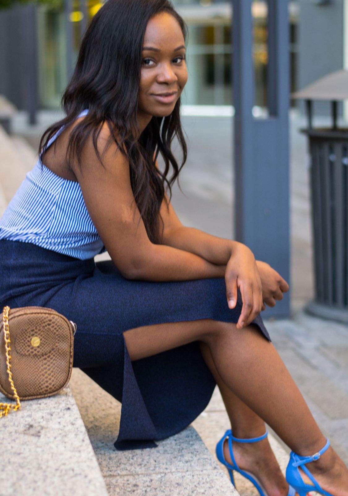 Client session photo: woman in a striped top and navy skirt seated on granite steps downtown