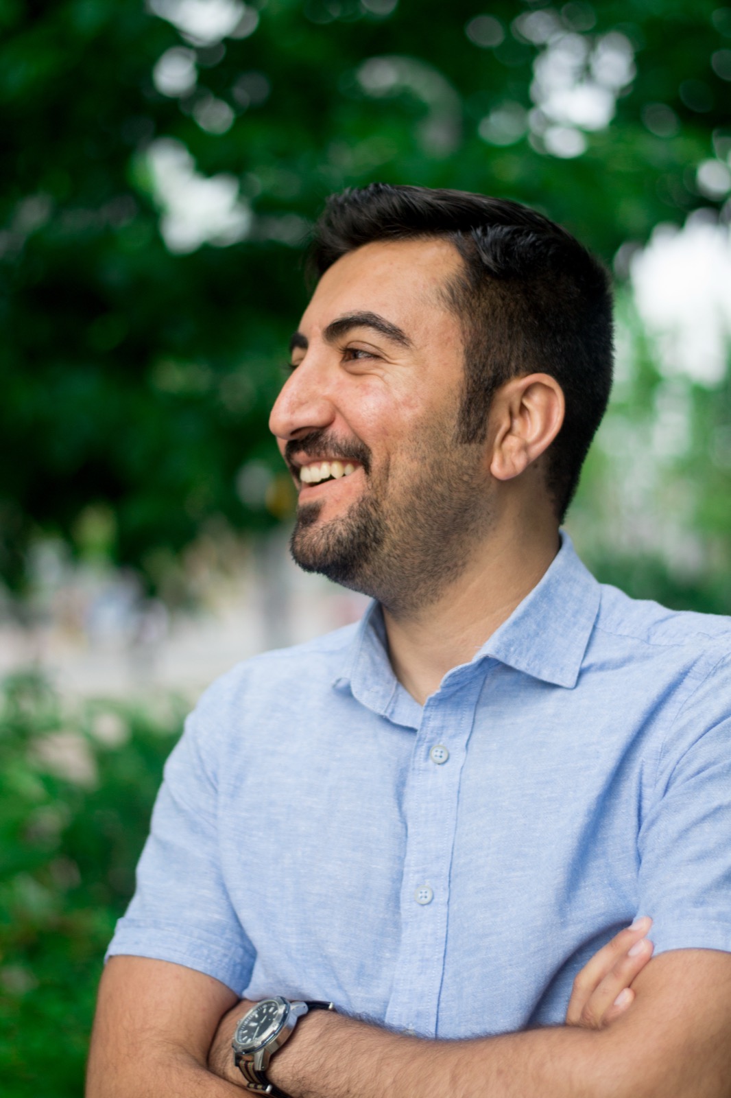 Client session photo: man in a light blue shirt laughing in a leafy city park