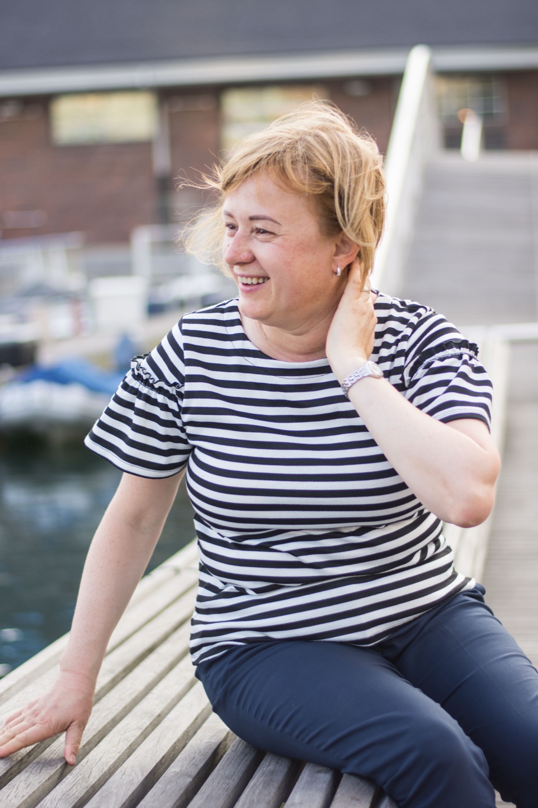 Client session photo: woman in a striped tee laughing on a dockside boardwalk bench
