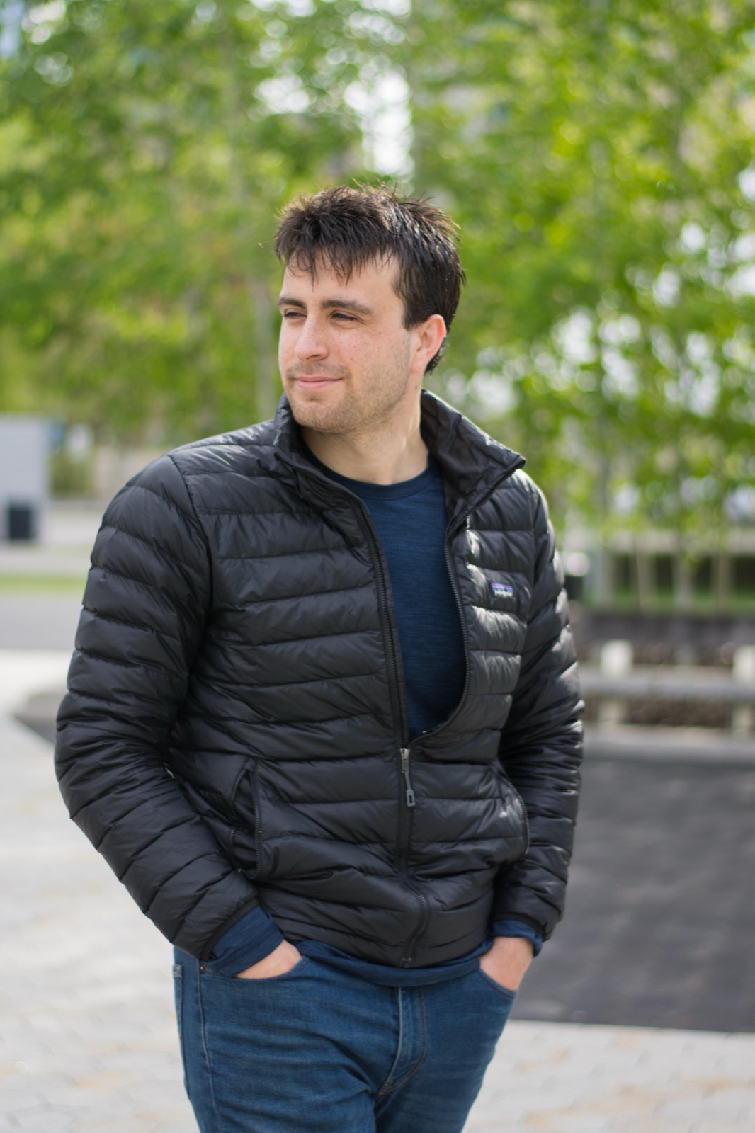 Client session photo: man in a black puffer jacket and jeans among trees in a city park