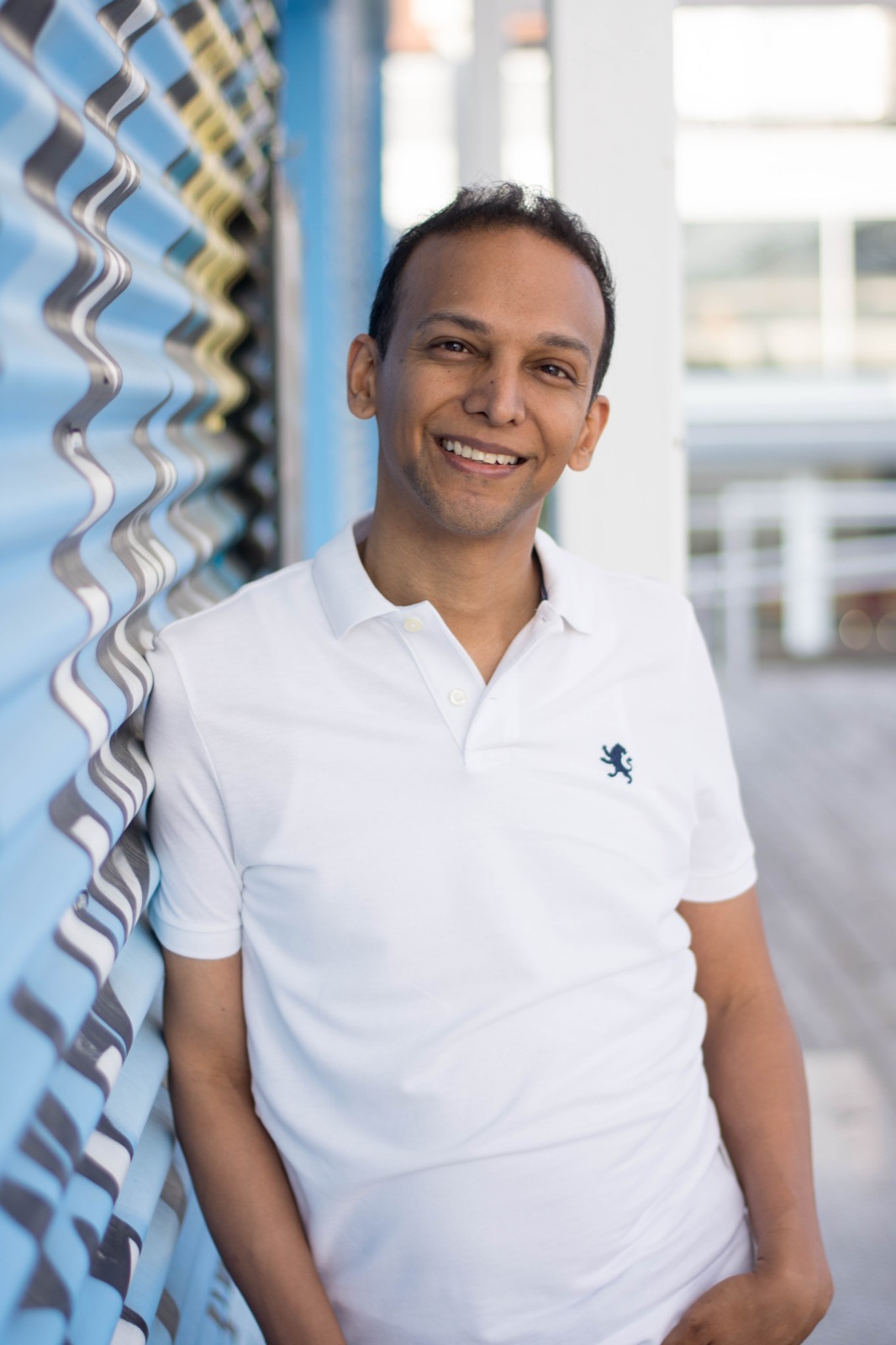Client session photo: man in a white polo smiling against a light blue corrugated wall