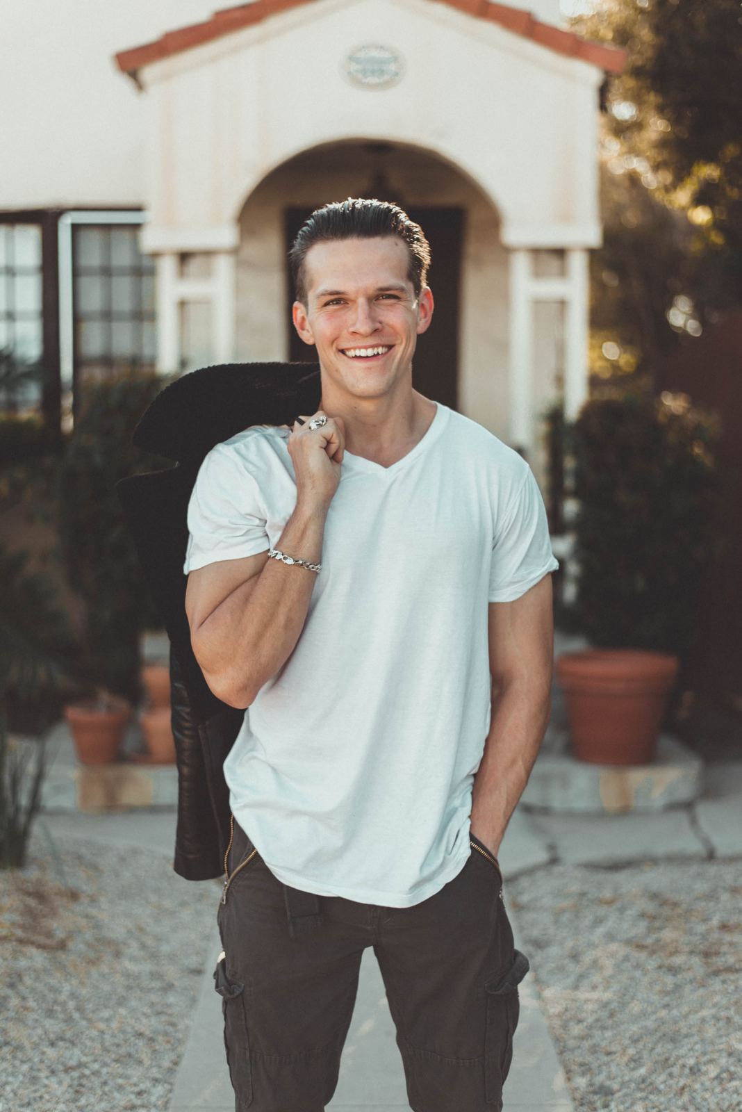 Client session photo: man in a white t-shirt with a jacket over his shoulder, smiling in front of an arched doorway