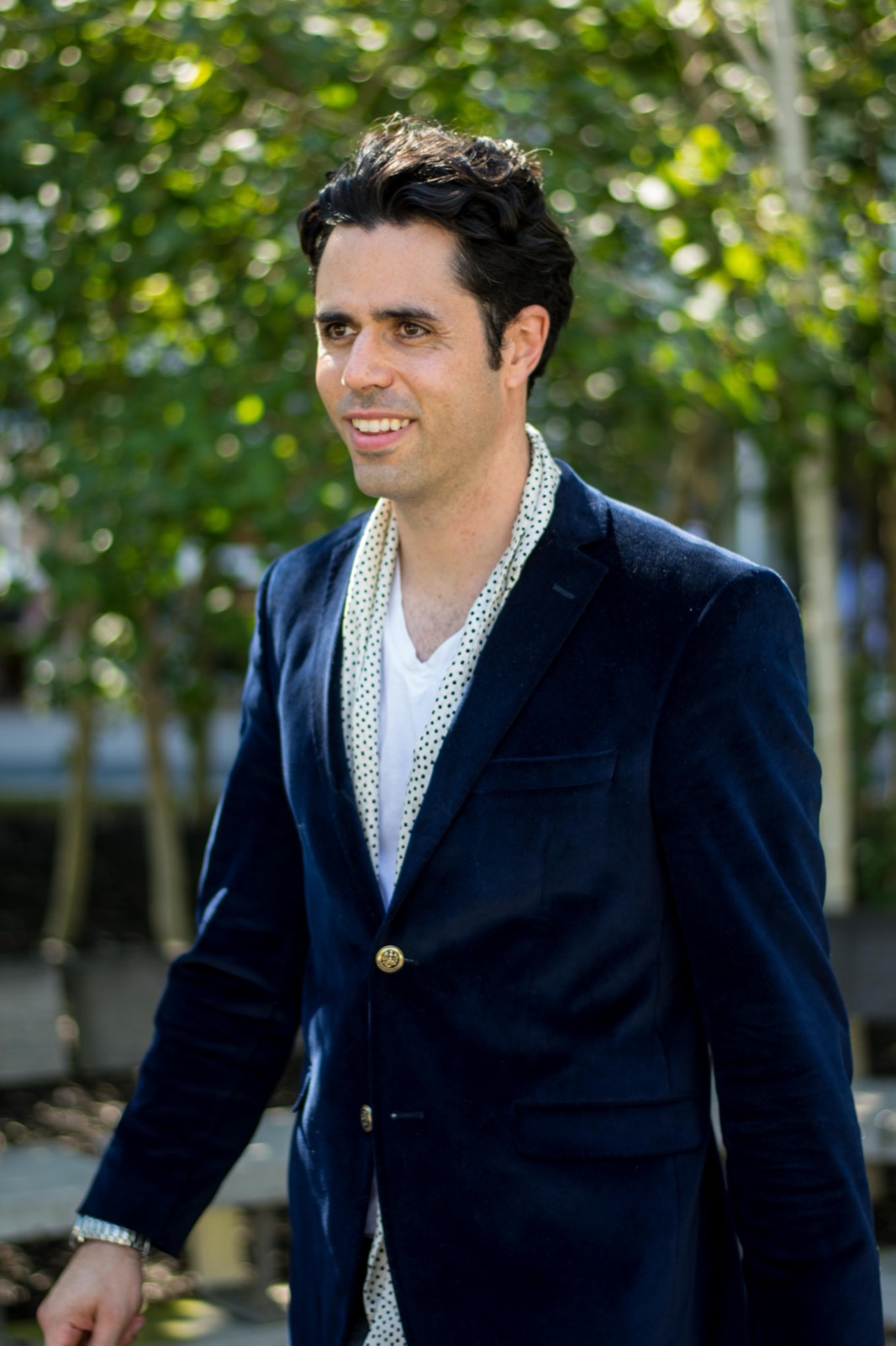Client session photo: man in a navy velvet blazer and white tee walking along a tree-lined path