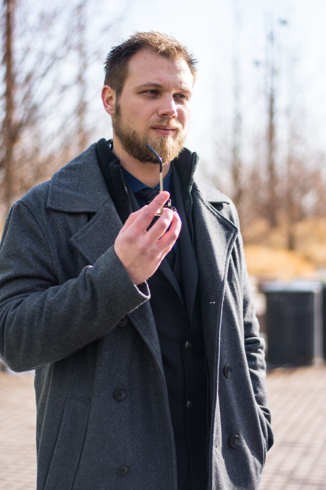 Client session photo: bearded man in a grey wool peacoat holding his sunglasses on a winter street